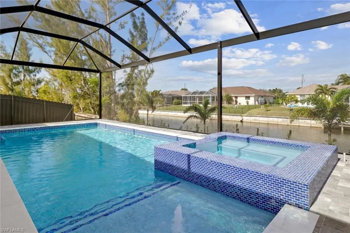 View of pool with a patio area, glass enclosure, and an in ground hot tub