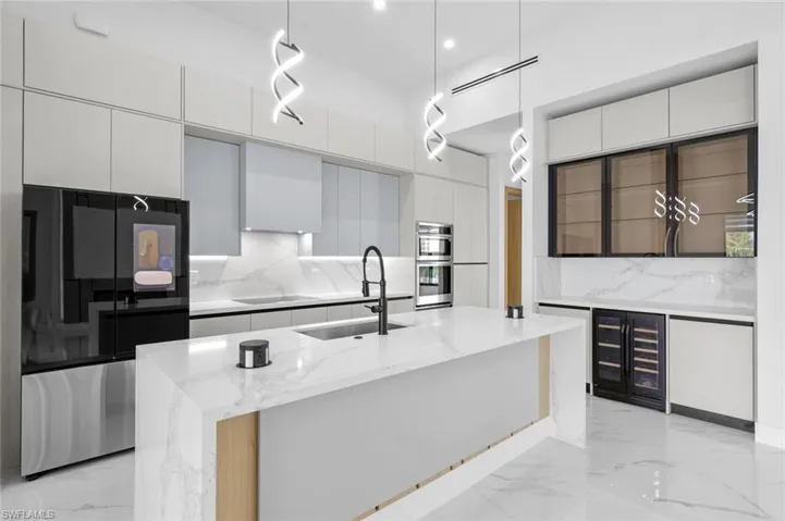 Kitchen featuring a center island with sink, appliances with stainless steel finishes, decorative backsplash, hanging light fixtures, and sink