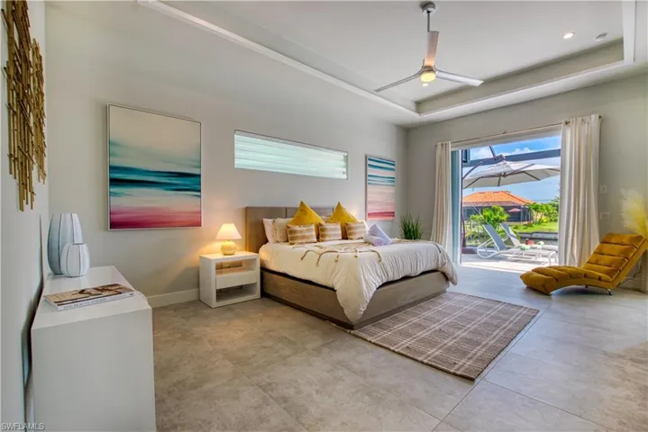 Tray ceiling with a modern ceiling fan in a room featuring large format tile flooring and a sliding glass door providing direct access to an outdoor patio with lounge chairs