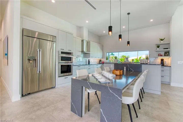 Modern kitchen featuring light gray cabinetry, stainless steel appliances, a waterfall island with integrated dining, recessed lighting, and a panoramic window