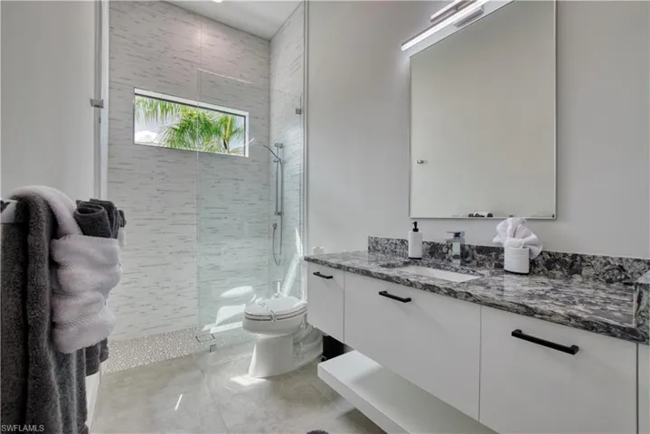 Contemporary bathroom featuring a floating double vanity with a dark granite countertop, a rectangular undermount sink, and a sleek wall-mounted mirror