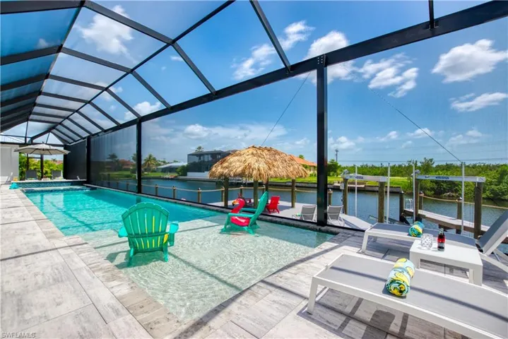 Screened enclosure featuring a large pool with an integrated sun shelf, a spa, and travertine-style decking