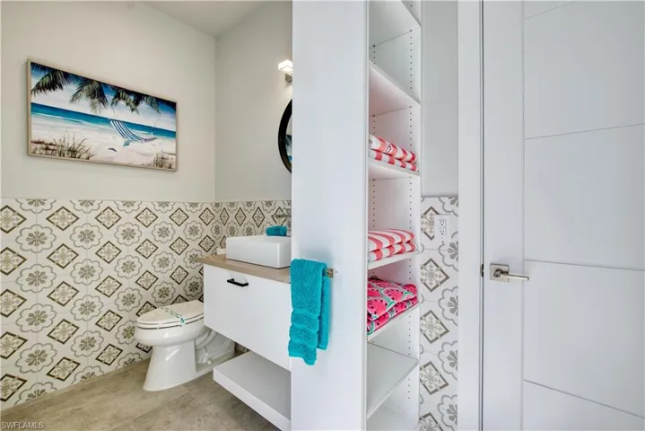 Powder room featuring decorative patterned wainscoting, a wall-mounted vanity with a vessel sink, and an integrated shelving unit
