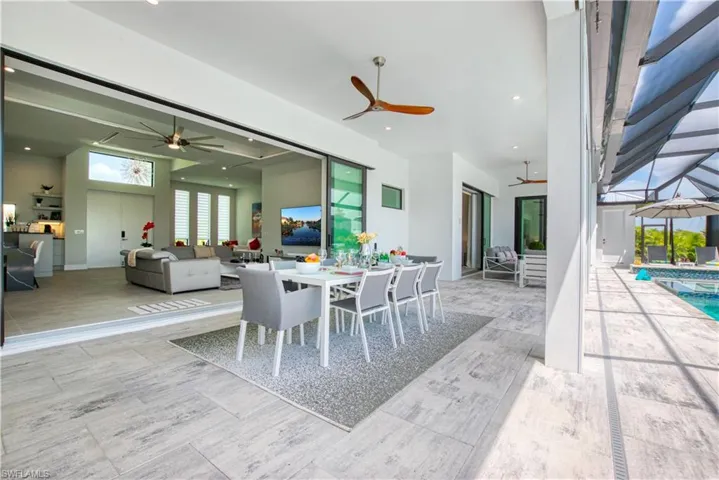 Expansive covered patio featuring light-toned large format tile flooring, multiple ceiling fans, recessed lighting, and direct access to the interior living area through wide sliding glass doors