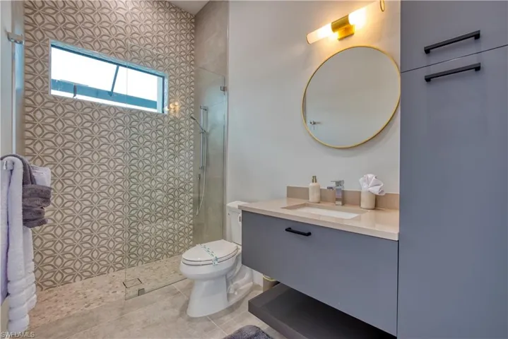 Modern bathroom featuring a walk-in shower with patterned tile, a floating vanity with a light-toned countertop, a contemporary round mirror, and built-in storage cabinetry