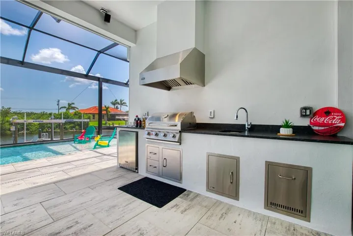 Outdoor kitchen featuring a built-in stainless steel grill, beverage refrigerator, stainless steel sink, and dark countertop