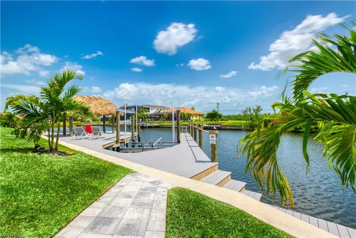 Waterfront property featuring a composite dock with integrated steps, a boat lift, and a thatched-roof tiki hut