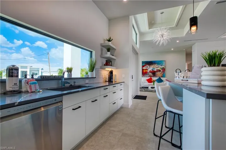 Modern kitchen featuring a horizontal picture window, dark countertop, white flat-panel cabinetry with matte black hardware, and stainless steel dishwasher