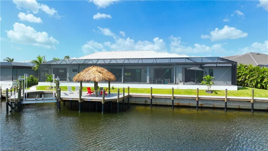 Waterfront property featuring a screened lanai, a private dock with boat lift, a tiki hut-covered patio, and a metal roof