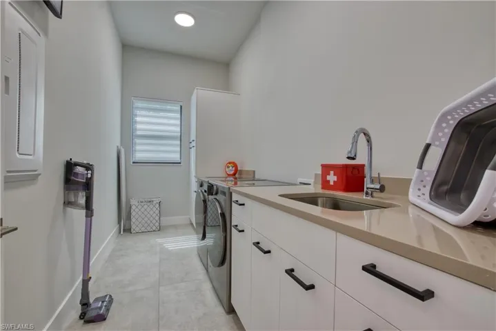 Modern utility room featuring a built-in sink with a gooseneck faucet, light-toned countertop, white cabinetry with black hardware, and light gray tile flooring