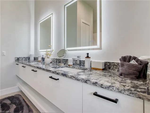 Dual vanity featuring a stone countertop with two undermount sinks, flanked by two backlit mirrors