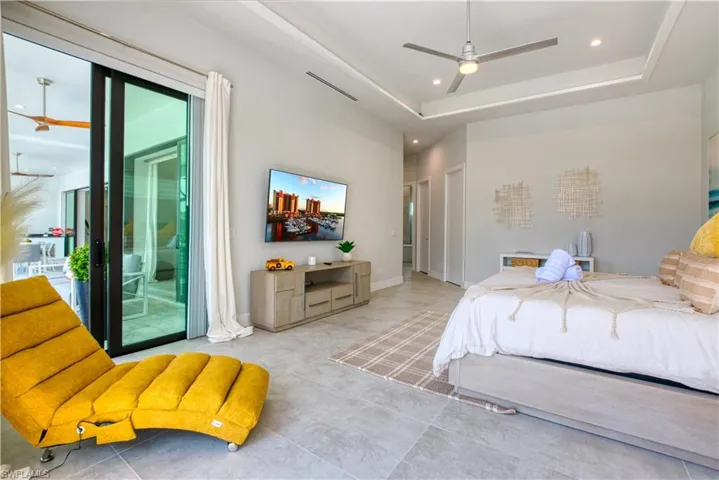 Spacious interior featuring large format tile flooring, a tray ceiling with recessed lighting and a ceiling fan, and sliding glass doors opening to an outdoor area