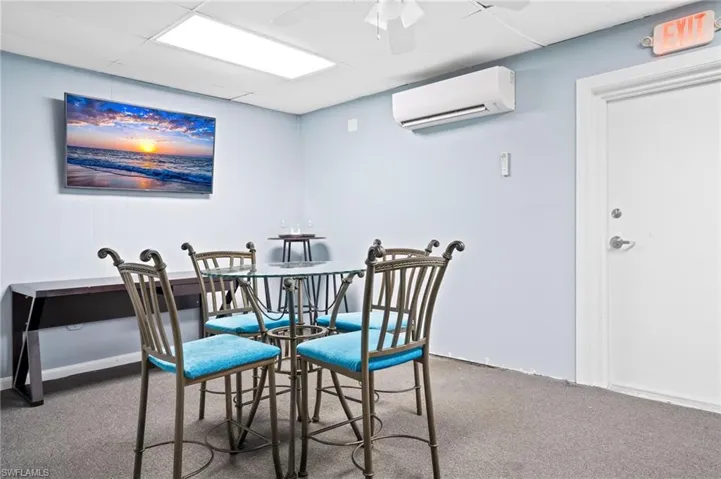 Break area with ceiling fan, a wall mounted AC, a drop ceiling, and carpet floors