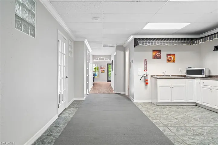 Hall with light tile patterned floors, a drop ceiling, sink, and ornamental molding