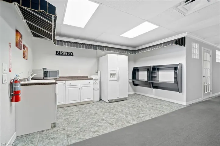 Kitchenette with white cabinetry, white fridge with ice dispenser, a paneled ceiling, and ornamental molding