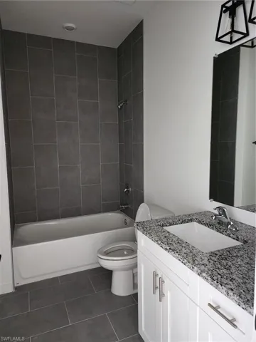 Full bathroom with vanity, bathing tub / shower combination, and dark tile patterned floors