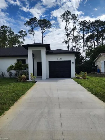 View of front facade featuring stucco siding, driveway, a front yard, and an attached garage