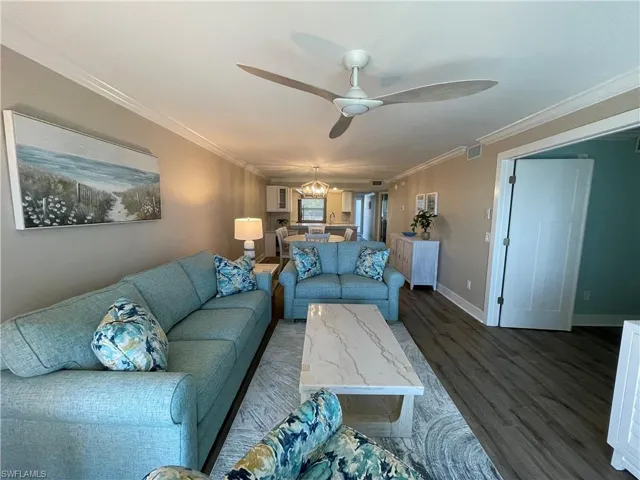 Living room featuring dark wood finished floors, ornamental molding, a ceiling fan, and a chandelier