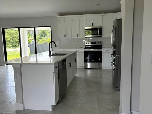 Kitchen with appliances with stainless steel finishes, white cabinetry, sink, and light tile floors