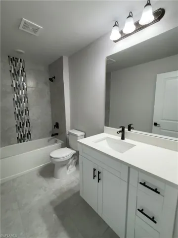 Full bathroom with tile flooring, tiled shower / bath combo, vanity, and toilet