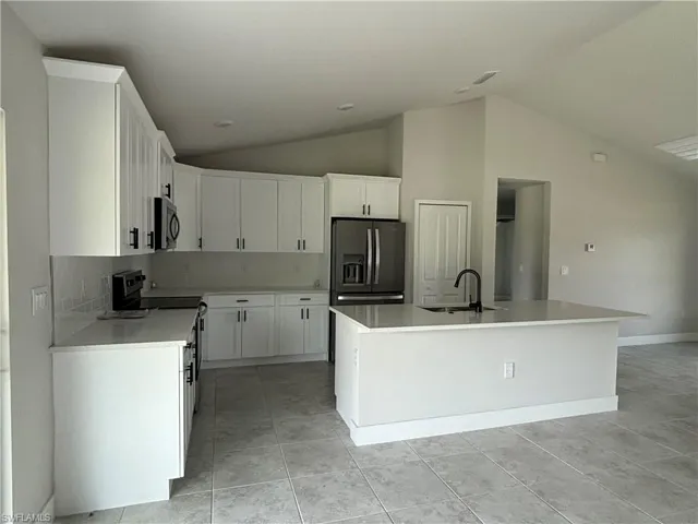 Kitchen with stainless steel appliances, a center island with sink, sink, and white cabinets