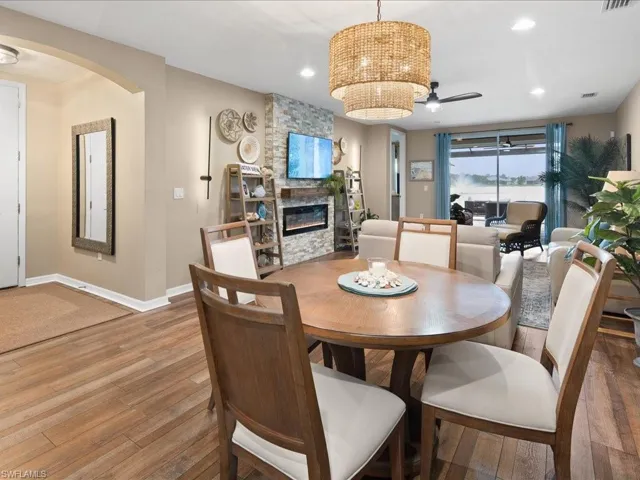 Dining space featuring a stone fireplace, wood-type flooring, and ceiling fan with notable chandelier
