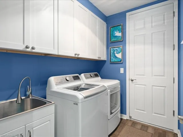 Clothes washing area featuring sink, cabinets, wood-type flooring, and washing machine and clothes dryer