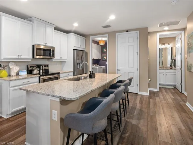 Kitchen featuring appliances with stainless steel finishes, white cabinets, a center island with sink, dark hardwood / wood-style floors, and independent washer and dryer