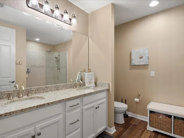 Bathroom with hardwood / wood-style flooring, a shower with door, toilet, and dual bowl vanity