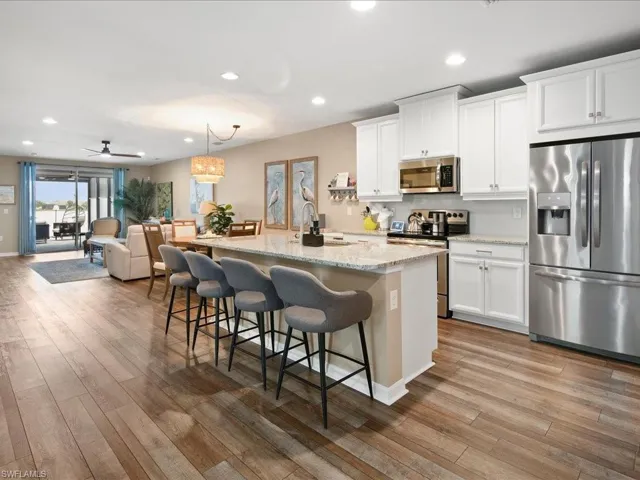Kitchen with white cabinetry, ceiling fan, stainless steel appliances, hardwood / wood-style floors, and decorative light fixtures