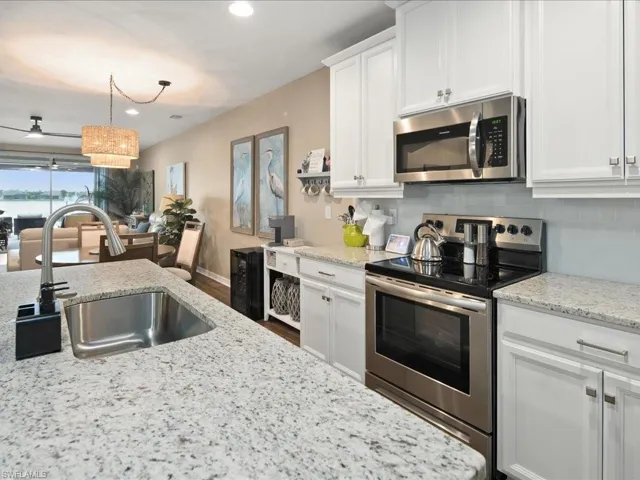Kitchen featuring appliances with stainless steel finishes, white cabinetry, light stone countertops, and sink
