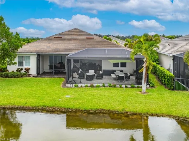 Back of house featuring a water view, glass enclosure, a patio area, and a yard