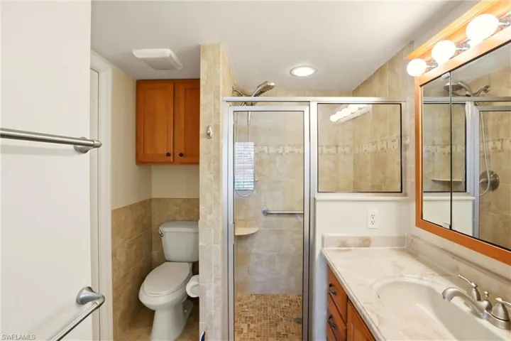 Bathroom featuring vanity, a stall shower, tile walls, a wainscoted wall, and light tile patterned floors