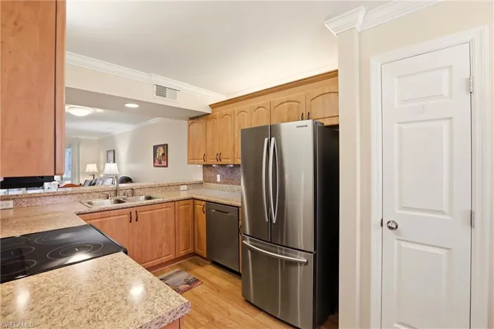 Kitchen featuring stainless steel appliances, light countertops, light wood finished floors, crown molding, and light brown cabinetry