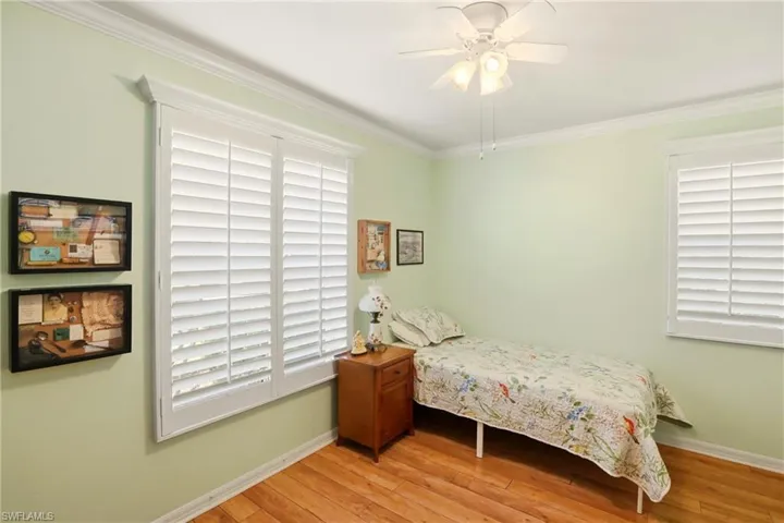 Bedroom with light wood-style flooring, crown molding, a ceiling fan, and multiple windows