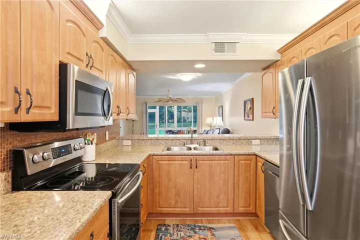 Kitchen featuring stainless steel appliances, crown molding, light wood-style floors, light stone counters, and a ceiling fan