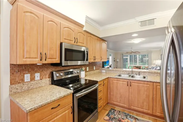 Kitchen with appliances with stainless steel finishes, light brown cabinets, ceiling fan, crown molding, and decorative backsplash
