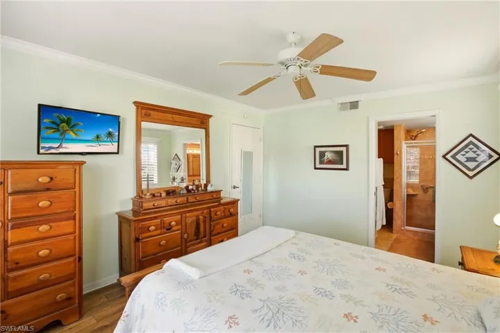 Bedroom with ornamental molding, wood finished floors, ceiling fan, and ensuite bath