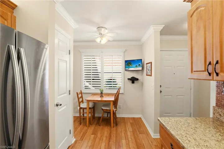 Kitchen featuring freestanding refrigerator, ornamental molding, light wood-style floors, ceiling fan, and light stone countertops