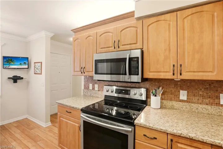 Kitchen featuring appliances with stainless steel finishes, ornamental molding, light brown cabinets, backsplash, and light stone countertops