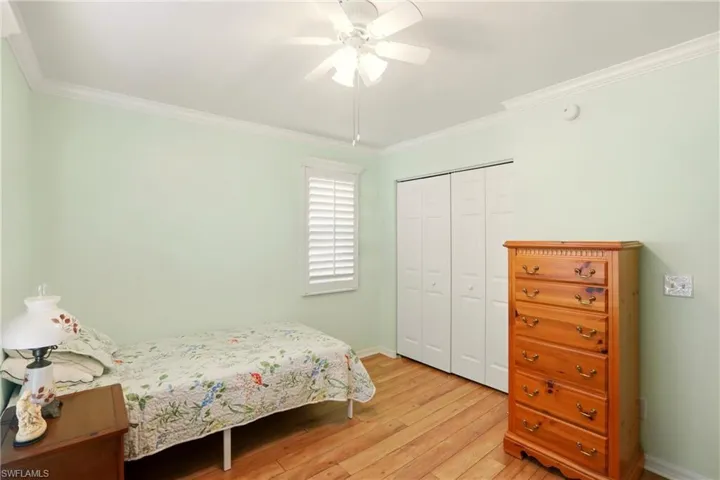 Bedroom with a closet, light wood finished floors, ceiling fan, and crown molding