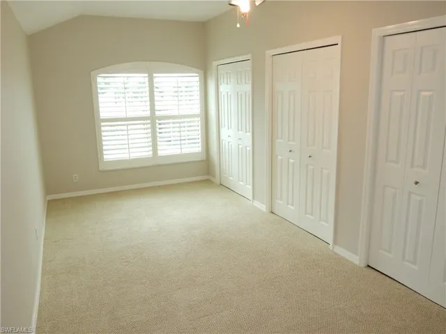 Arched window with plantation shutters, vaulted ceiling, built-in ceiling fan, light-toned carpeting, and multiple bi-fold closet doors