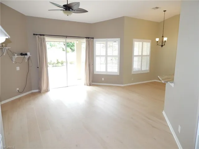Vaulted ceilings with a ceiling fan, light wood-finish flooring, sliding glass door, multiple windows with plantation shutters, and a breakfast bar with a stone countertop