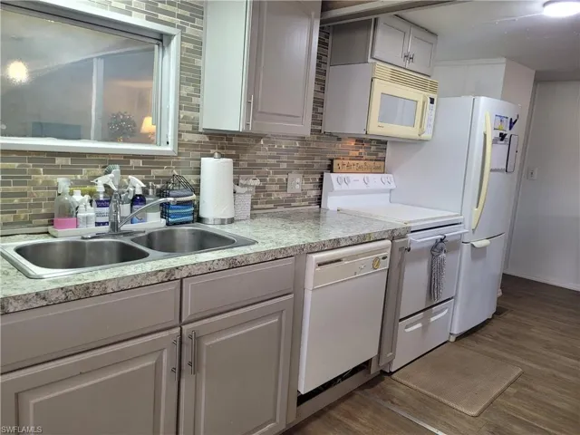 Kitchen featuring white appliances, backsplash, sink, and wood-style floors