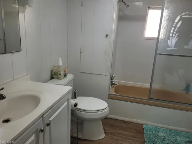 Full bathroom featuring vanity, toilet, hardwood / wood-style flooring, and bath / shower combo with glass door