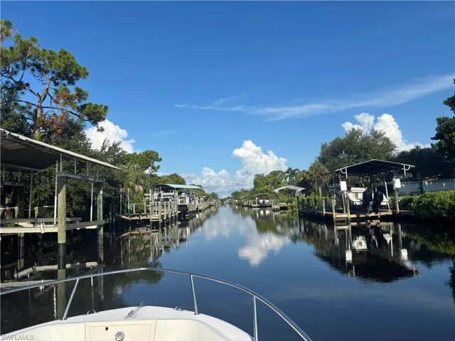 Waterfront property featuring a private boat dock with direct canal access, mature landscaping with native trees, and serene water views from the covered dock area