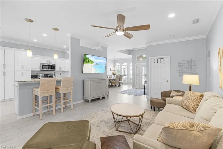 Open-concept living area featuring light wood-finish flooring, a contemporary ceiling fan, and crown molding