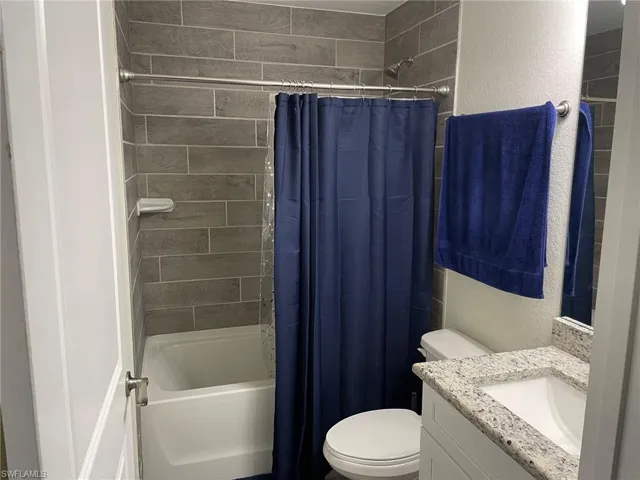 Bathroom featuring a textured wall, shower / bath combination with curtain, and vanity