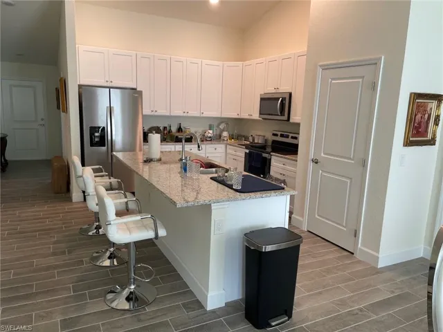 Kitchen featuring white cabinetry, stainless steel appliances, wood tiled floors, light stone counters, and a breakfast bar