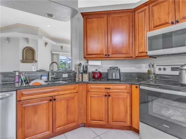 Kitchen featuring stainless steel appliances, crown molding, dark stone counters, a textured ceiling, and light tile patterned flooring
